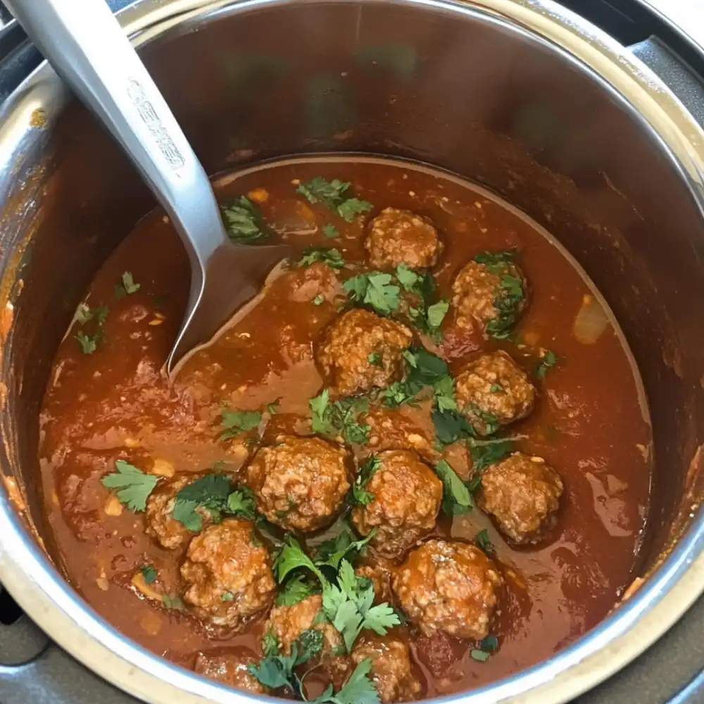 Pressure-cooked beef meatballs in tomato sauce, topped with cilantro, with a spoon inside the cooking pot.